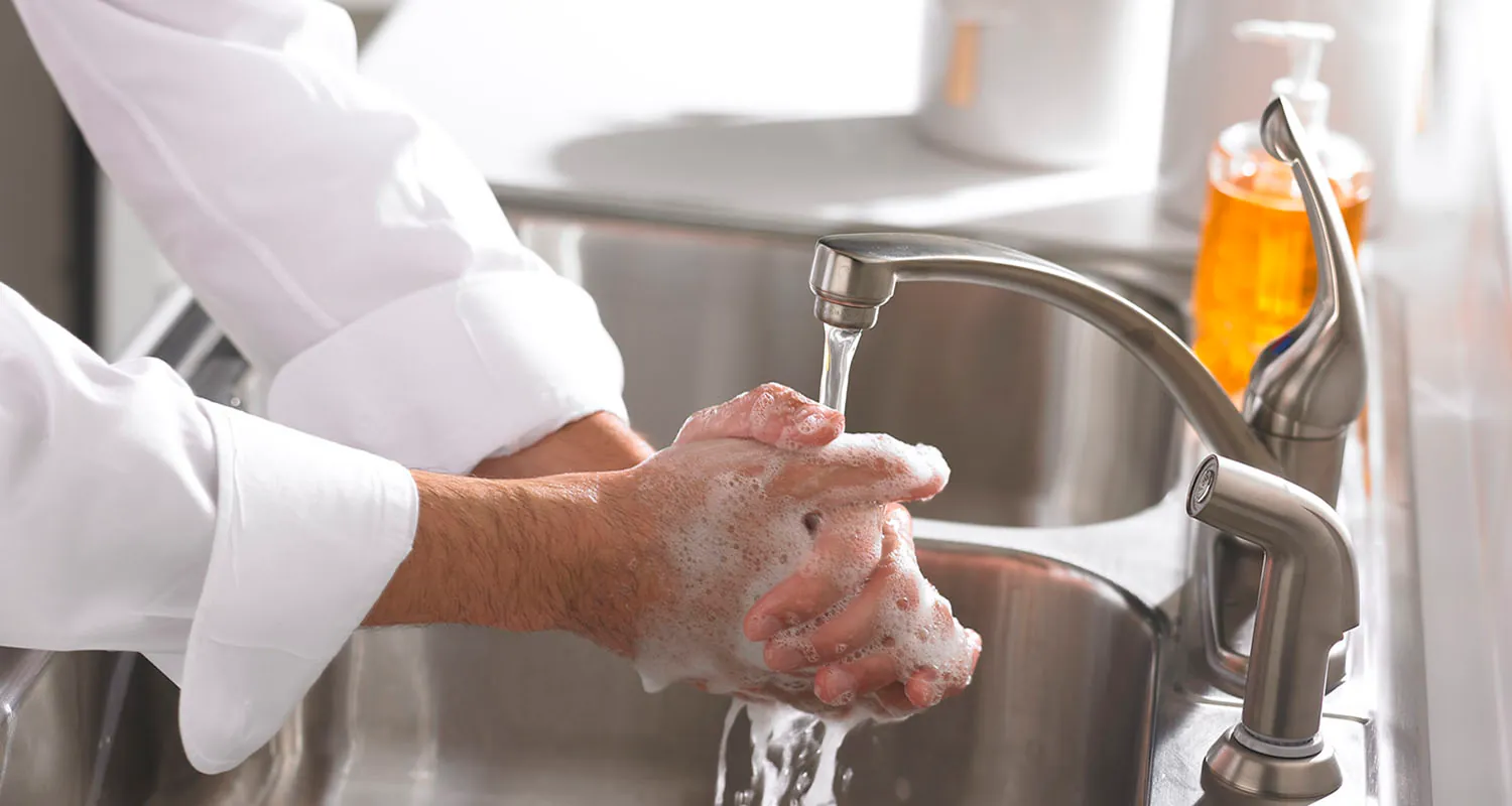 A photograph of a healthcare worker washing hands with soap in a sink is shown.
