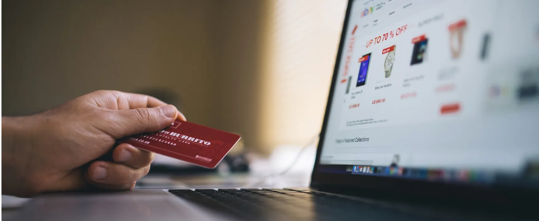 A photograph shows a person sitting at a laptop that is open to e bay. He is holding a member's loyalty credit card in his hand.