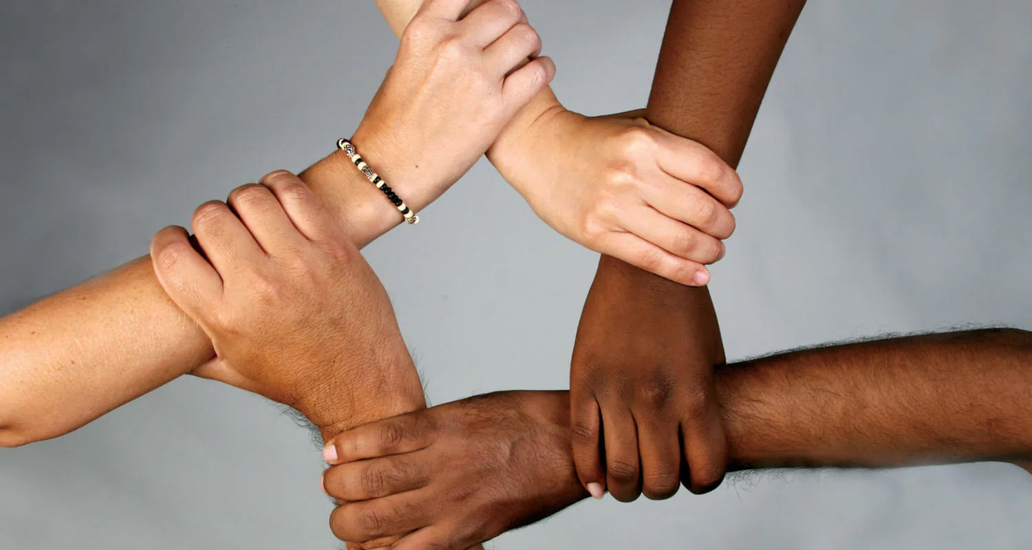 A photograph shows four people's hands holding each other's wrists.