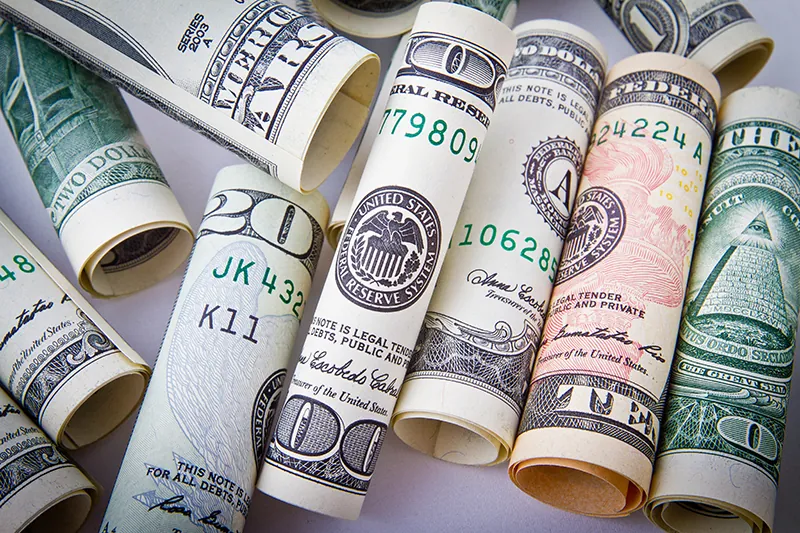 Rolled cash bills of various denominations, including 10, 20, and 100 US dollars.