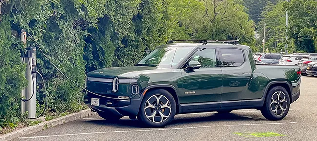 A photograph shows a parked Rivian vehicle plugged into a charging station.