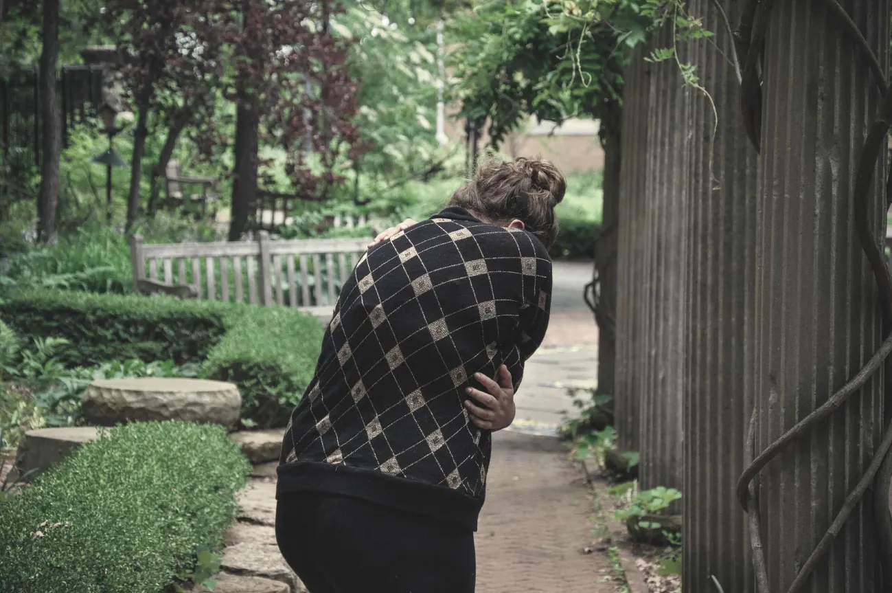 A color photograph shows a woman standing outside bent over and holding her body in pain.