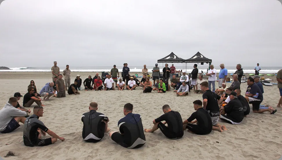 This photo depicts a large group of people sitting in a circle on the beach.