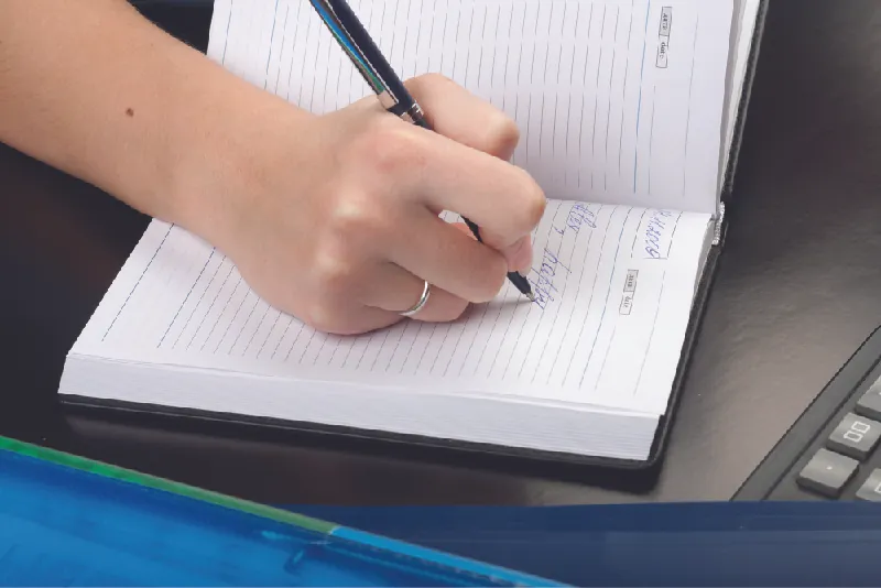 A photograph shows a person writing in a journal.