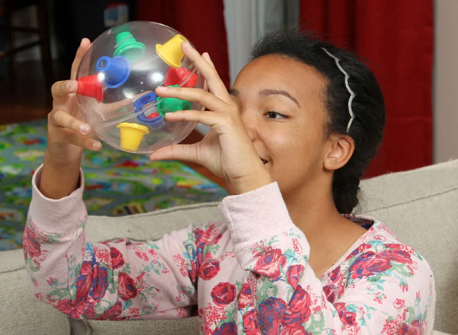 Photo of a child looking at a round toy while holding it up in the air.