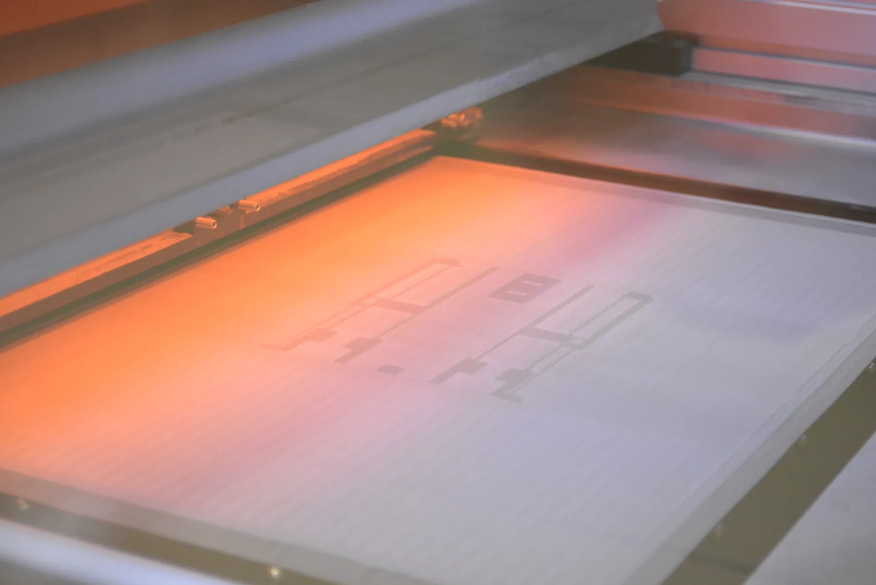 A binder bed printer is shown. A wide flat surface is lit up on one side, and there are outlines of shapes on the surface. 