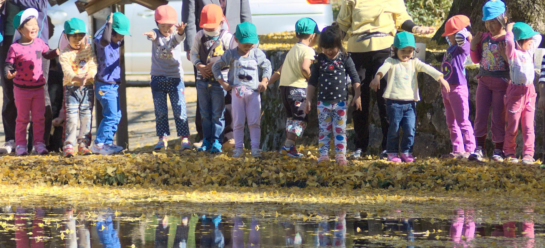 Photo of group of young children standing next to a leaf littered stream, with excited looks on their faces.