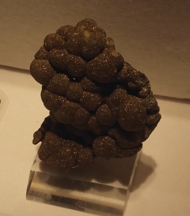 This figure shows a large, dull, black, lumpy mass with small, metallic flecks displayed on a clear, colorless rectangular solid base.