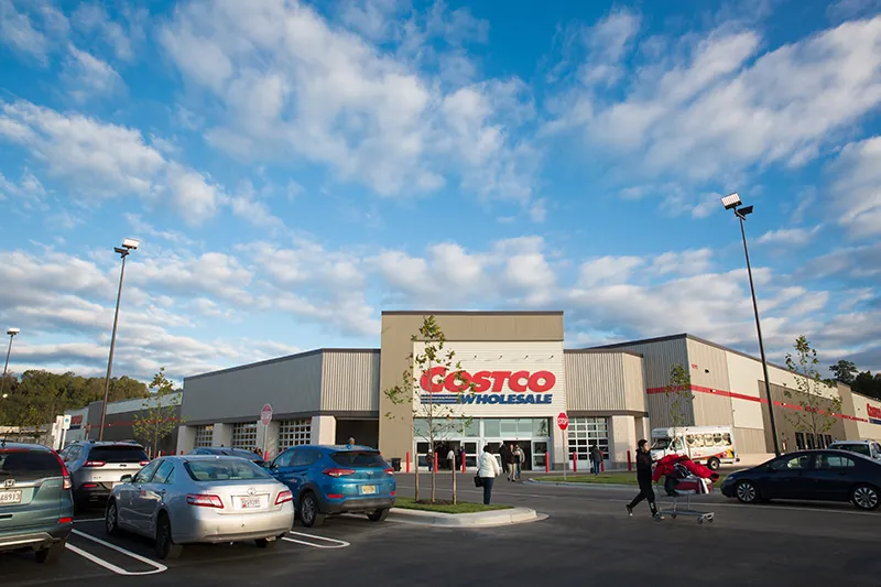 Witryna sklepu Costco przedstawia zaparkowane samochody i ludzi idących do i ze sklepu.