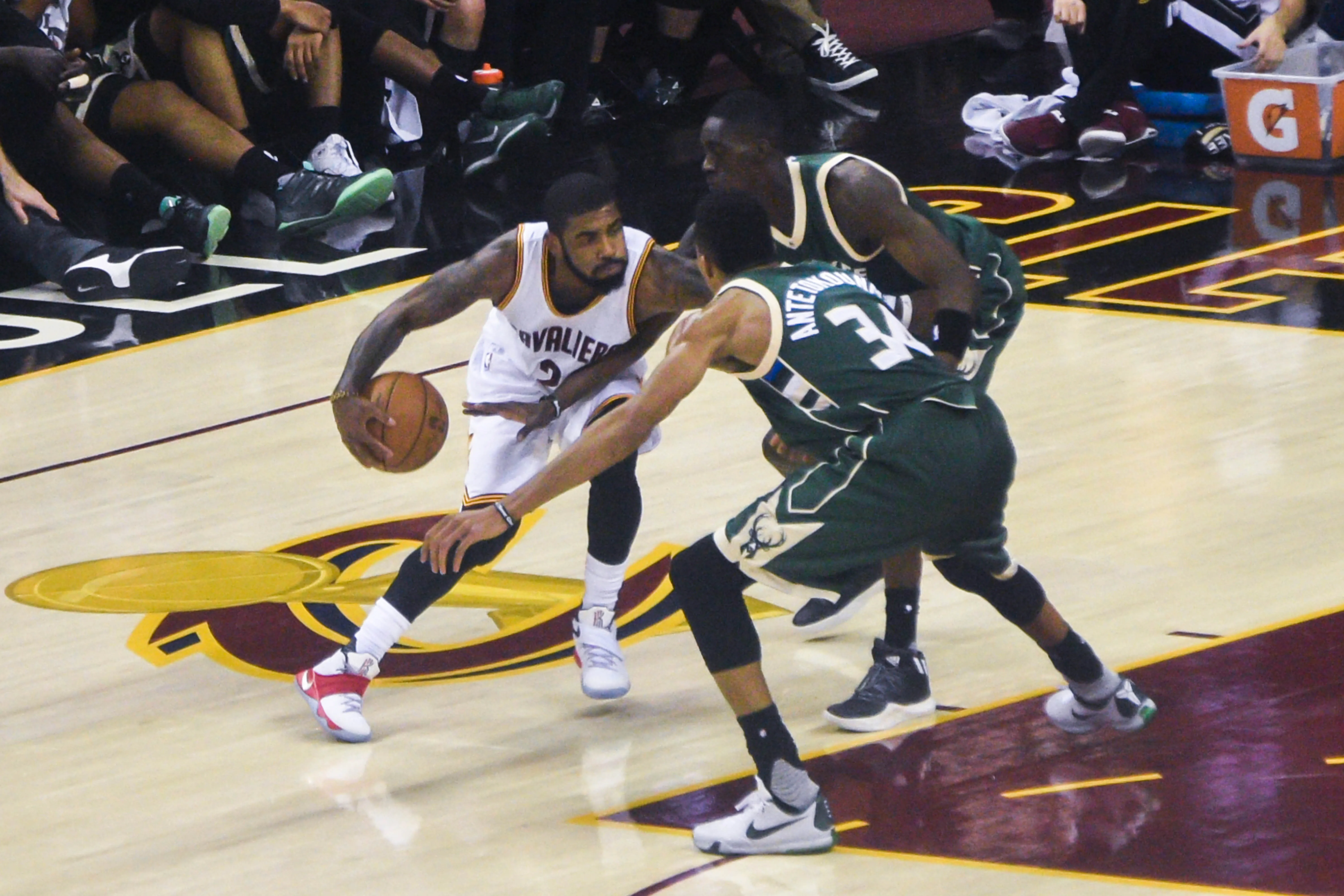 Cleveland Cavaliers' Kyrie Irving (No. 2) dribbles past two Milwaukee Bucks defenders, including Giannis Antetokounmpo (No. 34), on the basketball court during a game.