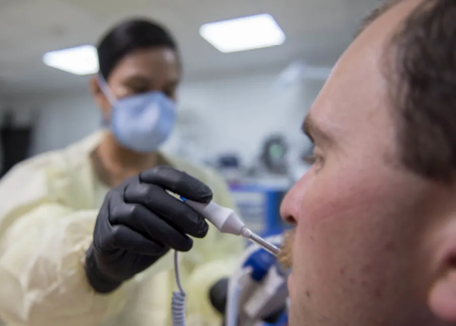 A photo of a provider placing a thermometer in a patient’s mouth.