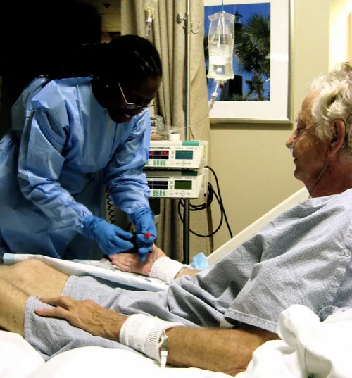 Photo of healthcare worker performing medical procedure on individual sitting in a hospital bed.