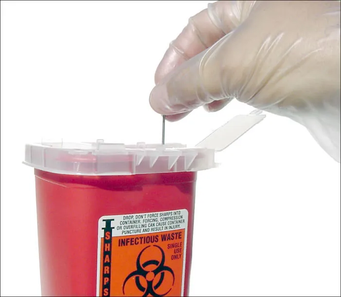 Gloved hand placing needle in container marked "sharps" and "infectious waste"