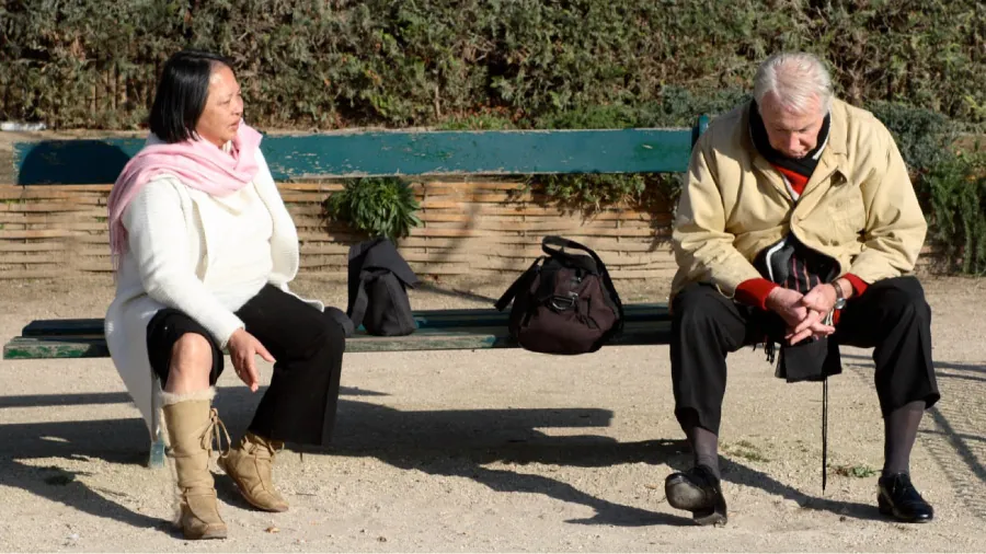 Photo of two individuals sitting on an outside bench talking.