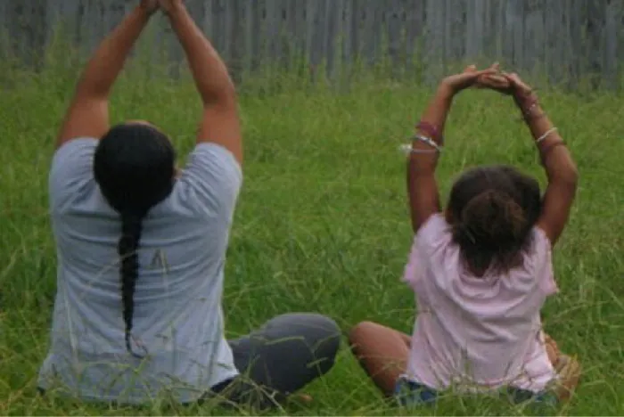Photo of adult and child sitting cross legged in the grass with their arms over their heads.