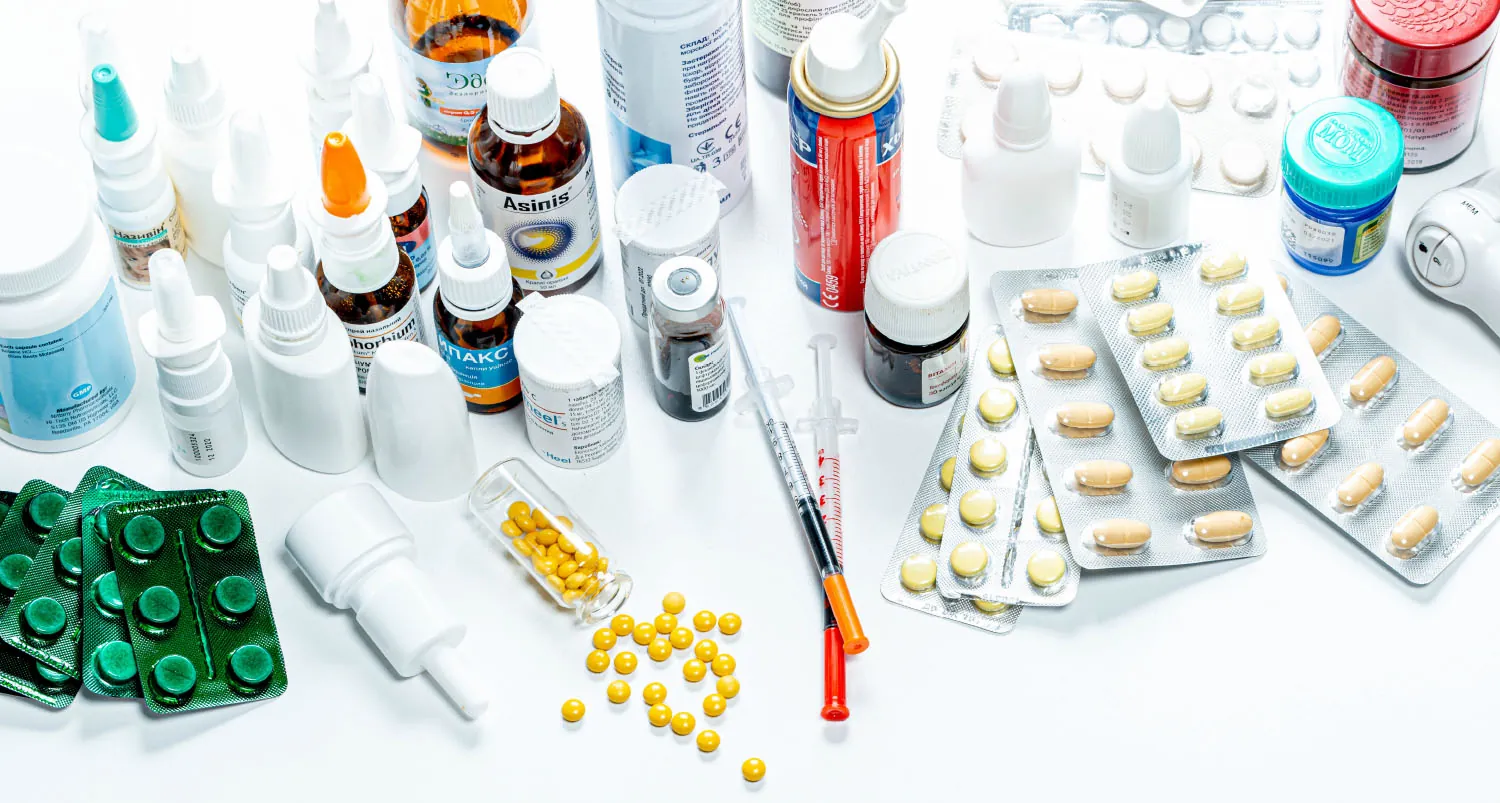 A photograph of various medications is shown. The medications include packets of pills, bottles of capsules, nose sprays, jars of topical creams, and syringes.