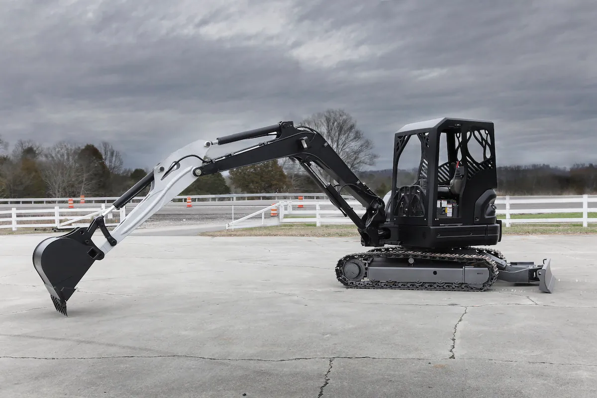 An excavator is shown with its boom extended. A one-person cab sits on top of track wheels, and a three-part arm fitted with hydraulics is extended, with a clawed scoop at the end.