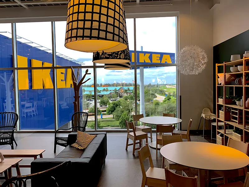 W salonie IKEA pokazana jest kanapa, dwa okrągłe stoły z krzesłami oraz regał.