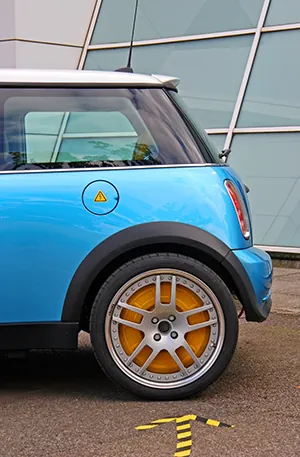 A side view of the back end of a blue compact car is shown. The car is sitting on black asphalt.