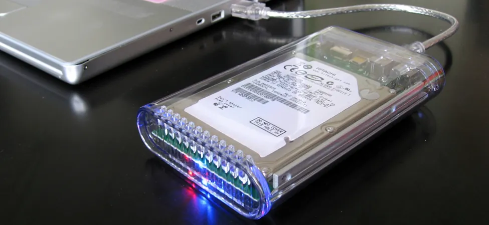 Zdjęcie pokazuje twardy dysk zewnętrzny podłączony do laptopa kablem i łączem USB.