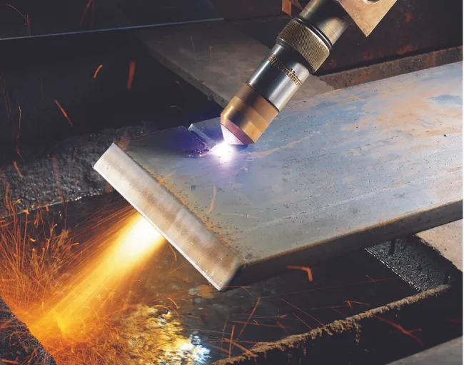 Se usa un soplete para cortar una pieza de metal. El plasma brillante y de color blanco se puede ver cerca de la punta de la antorcha, donde está en contacto con el metal.