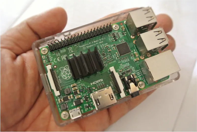 A hand holds the inside components of a computer part. The computer component has green, black, and silver pieces in various shapes with white words, images, and numbers on the green base.