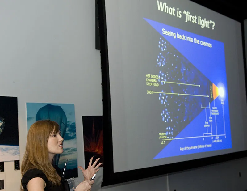 A student gives a presentation with the help of visual aids and other media, including a projector screen.