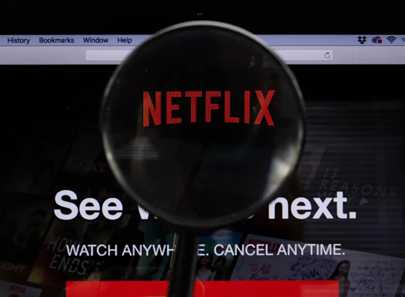 Zrzut ekranu strony Netflix przedstawia logo firmy. Nad słowem „Netflix” znajduje się szkło powiększające, które sugeruje możliwość odkrywania bogatej ofert firmy. Poniżej logo widnieje napis: „Zobacz, co będzie dalej. Oglądaj wszędzie. Anuluj w każdej chwili”.