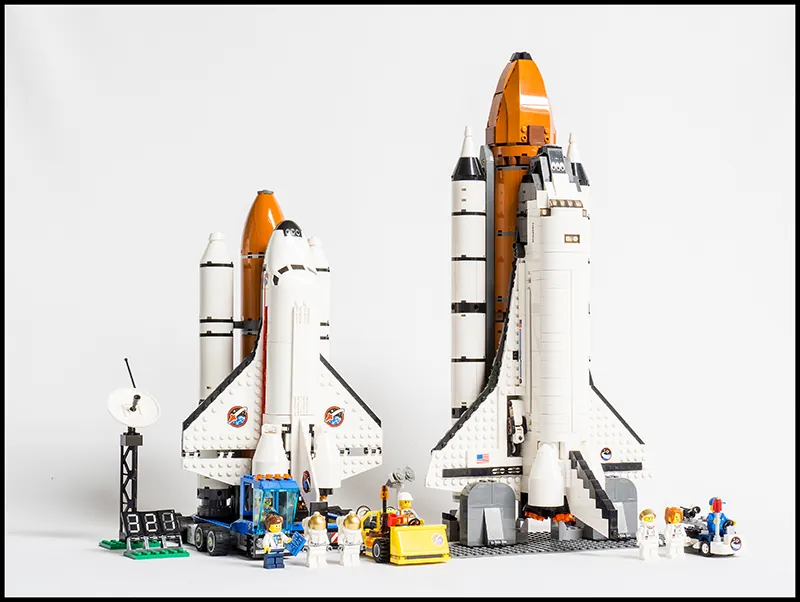 Dwa promy kosmiczne zbudowane z klocków Lego. Przed promami znajdują się mini figurki astronautów obu płci.