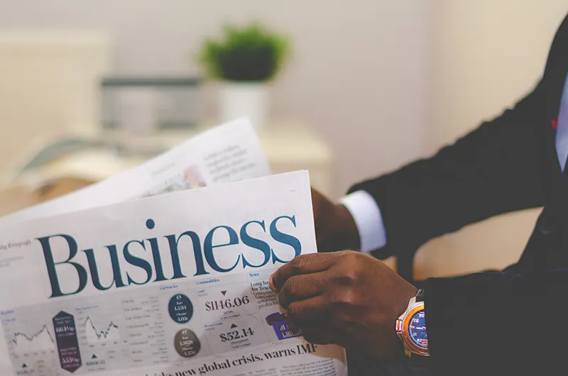Two arms are shown holding a business newspaper.